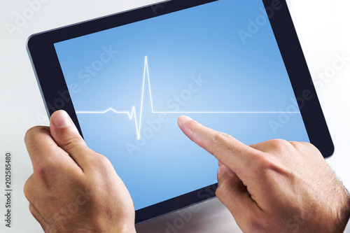 Man using tablet pc against medical background with blue ecg line