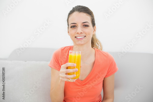 Beautiful calm woman smiling at camera holding a glass of orange juice