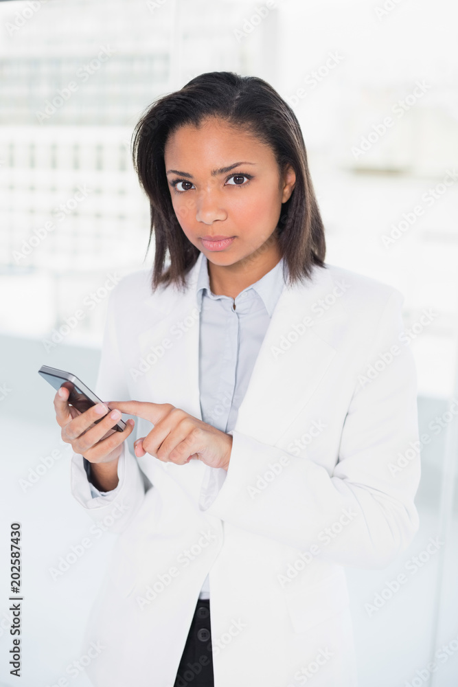 Obraz premium Stern young dark haired businesswoman using a mobile phone