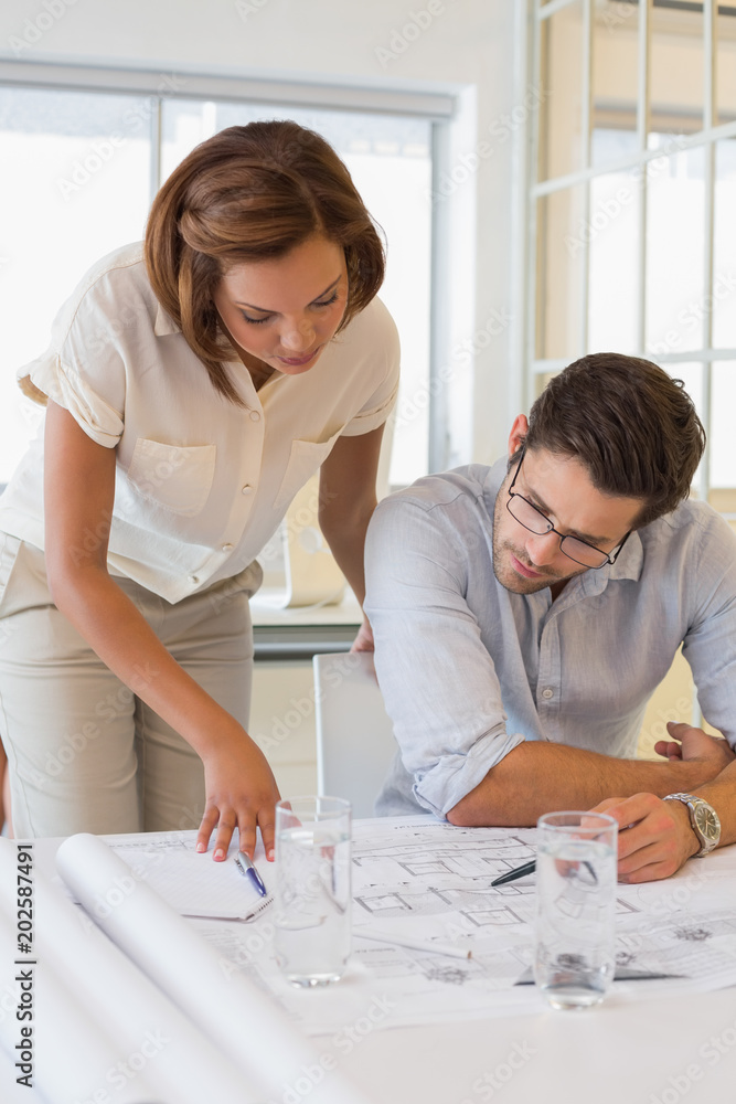 Concentrated colleagues working on blueprints at office Concentrated colleagues working on blueprints at office