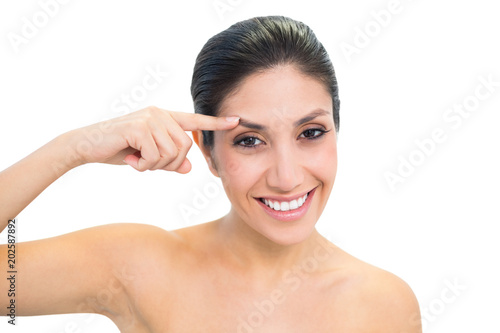 Happy brunette pointing to forehead and looking at camera