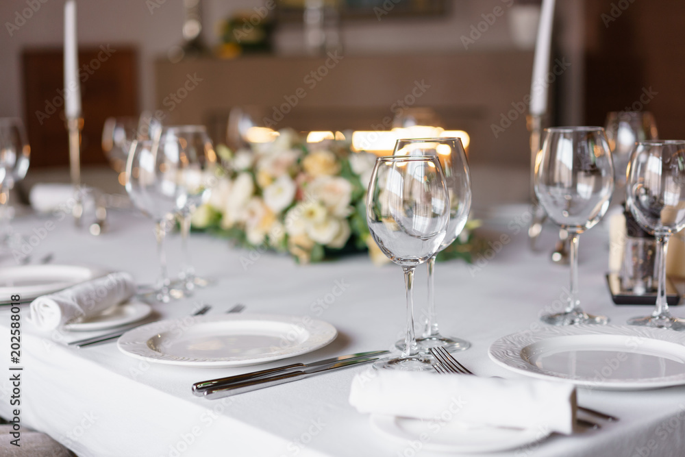Table setting in the restaurant, glasses in the foreground. Luxury wedding reception. Flower arrangement on table in restaurant. Stylish decor and adorning.