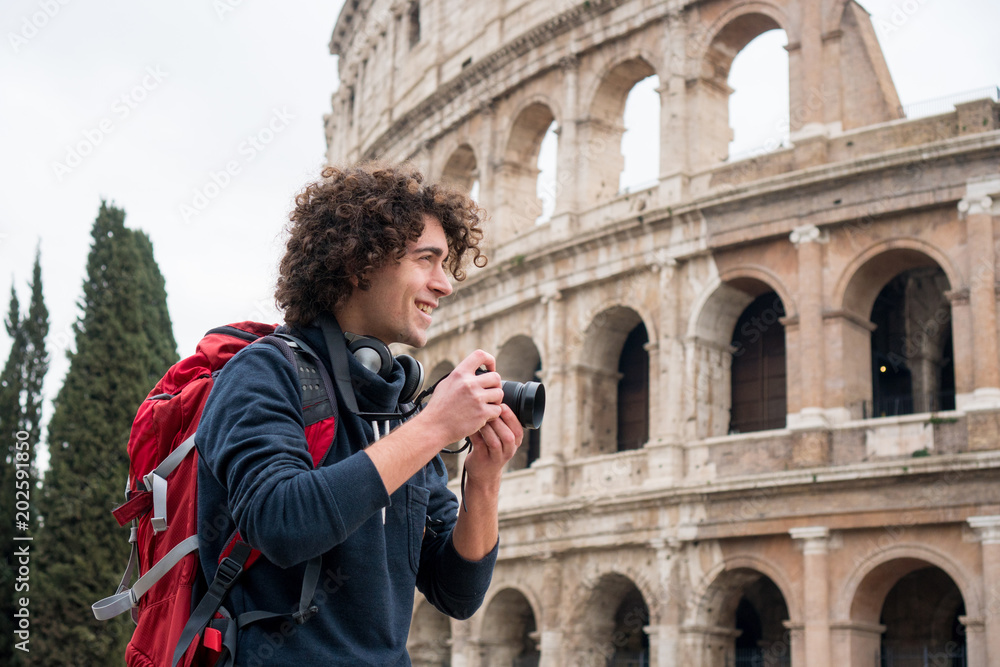 Φωτογραφία Handsome young tourist man with a camera and backpack taking pictures of Colosseum in Rome, Italy