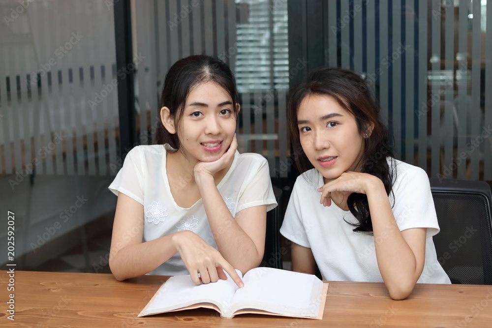 Attractive young Asian women with a book looking at camera in living room. Attractive young Asian women with a book looking at camera in living room.