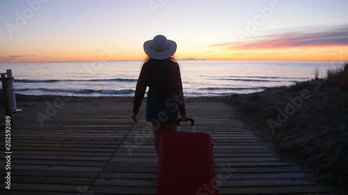 Young woman walking with a suitcase on the beach photo