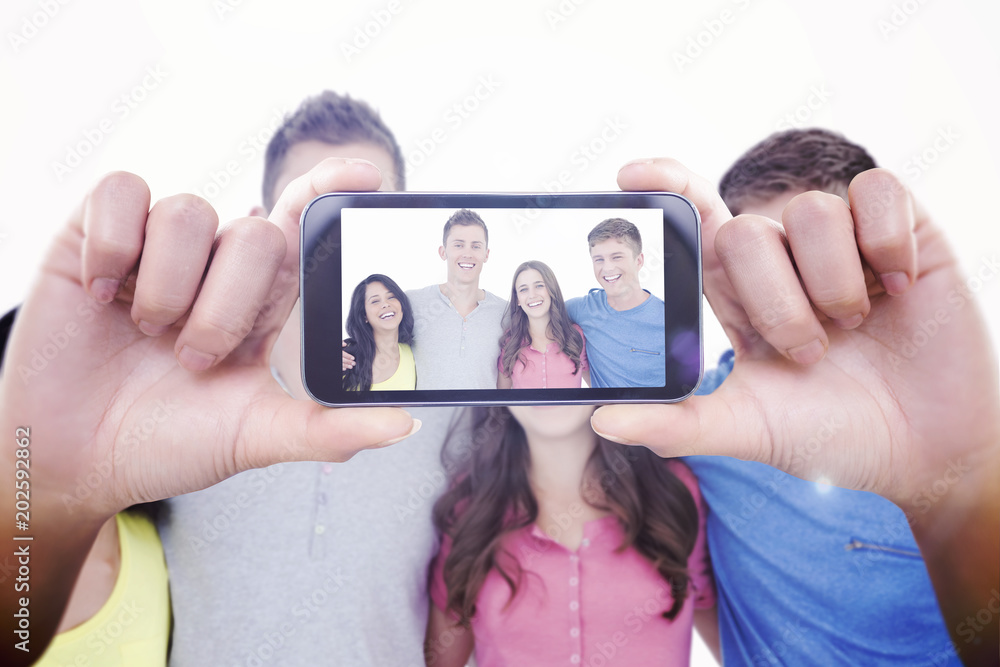 Hand holding smartphone showing against a laughing group of friends look at the camera 