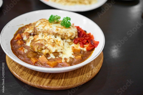 Delicious Japanese hamburg curry Serve with and mozzarella cheese on top with Rice, curry Rice in white plate on a black table with copy space.   