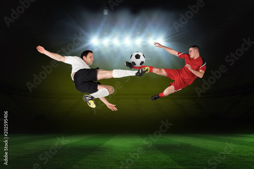 Football players tackling for the ball against football pitch under spotlights