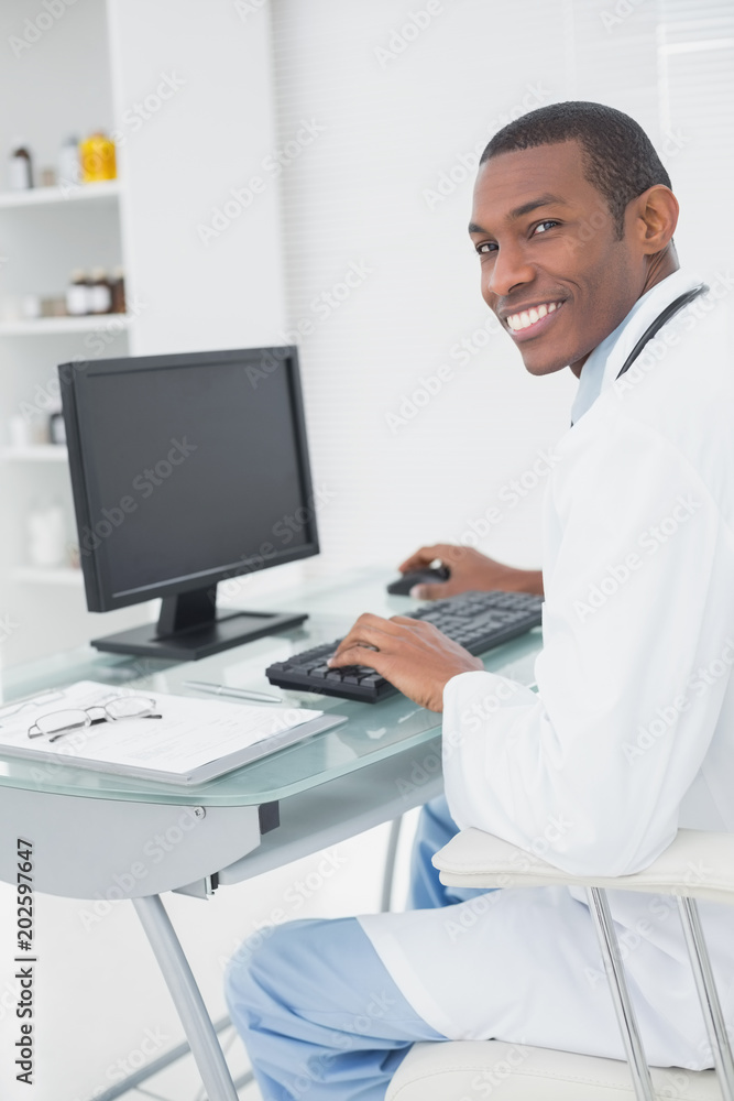 Smiling male doctor using computer at medical office