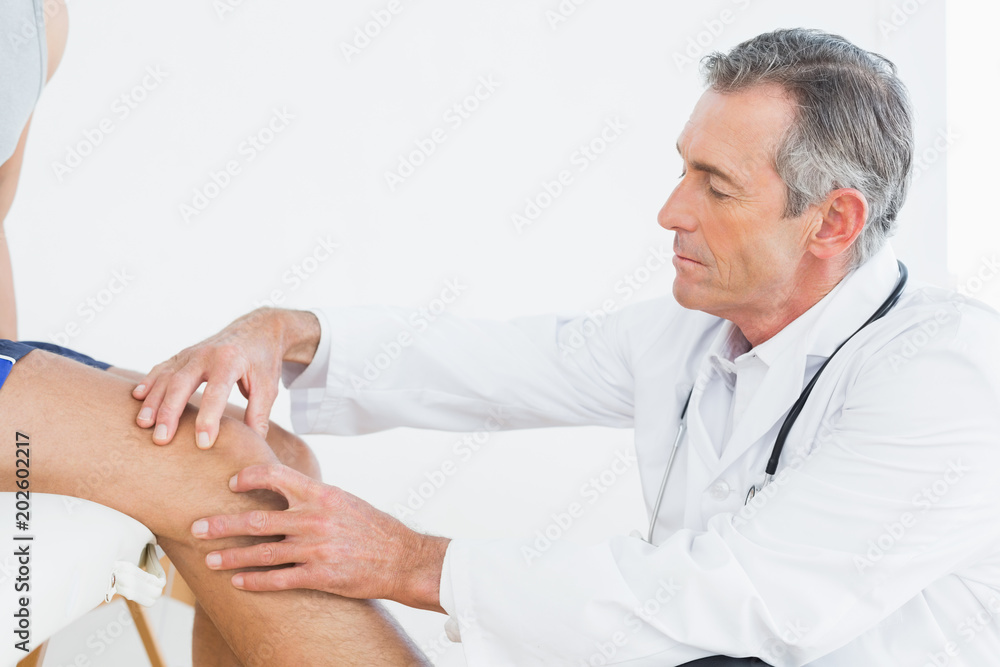 Fototapeta premium Side view of a mature doctor examining patients knee