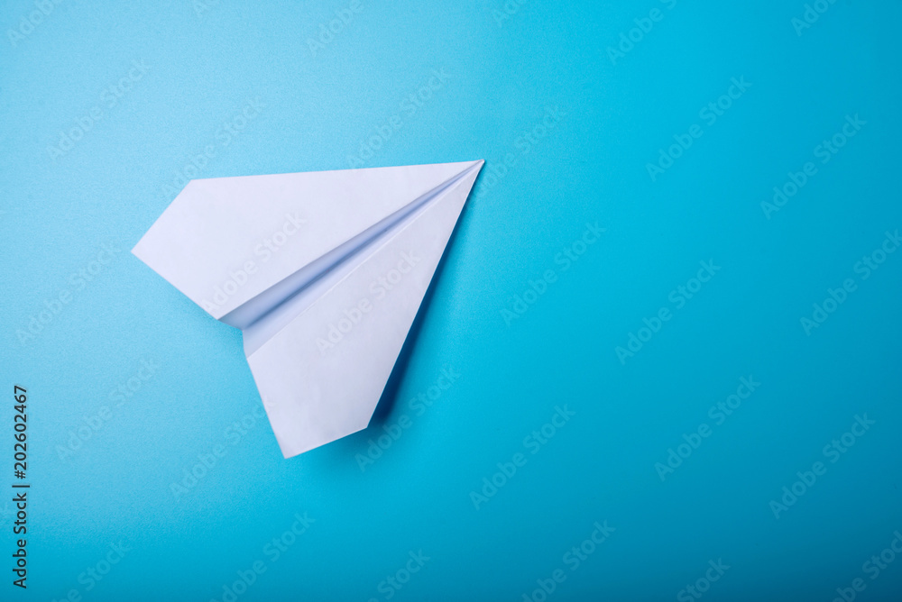 White paper origami airplane lies on pastel blue background White paper origami airplane lies on pastel blue background