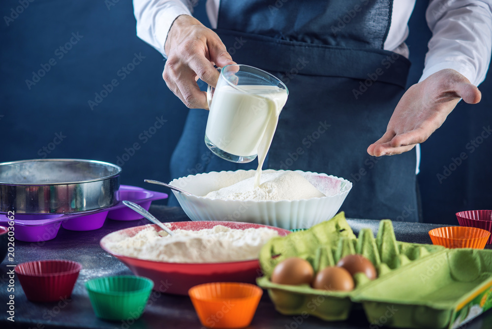 Chef pastry in a black apron in the process of making cupcakes from ingredients. Concept of confectionery cooking Chef pastry in a black apron in the process of making cupcakes from ingredients. Concept of confectionery cooking