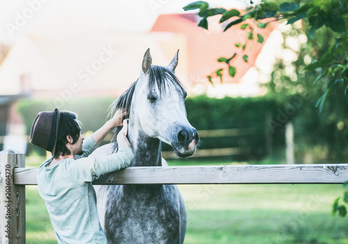Young guy scratches his horse at summer outdoor nature