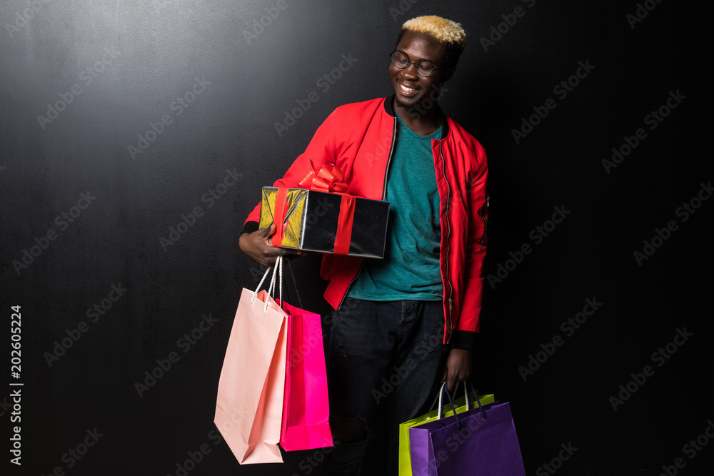 Obraz na plátně African American man with colorful paper bags and gift isolated on black backgro