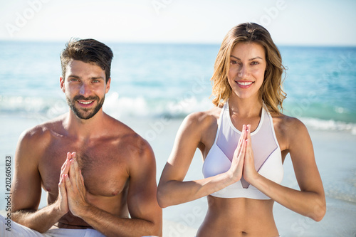 Portrait of young couple meditating while sitting on shore