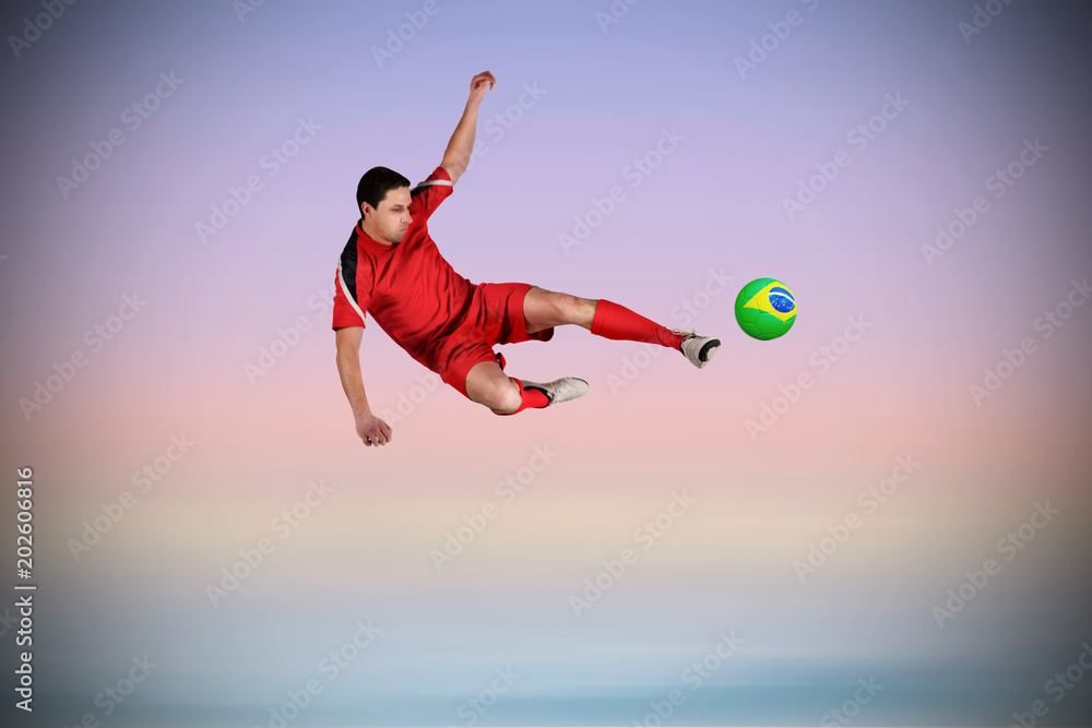 Fit football player jumping and kicking against purple background