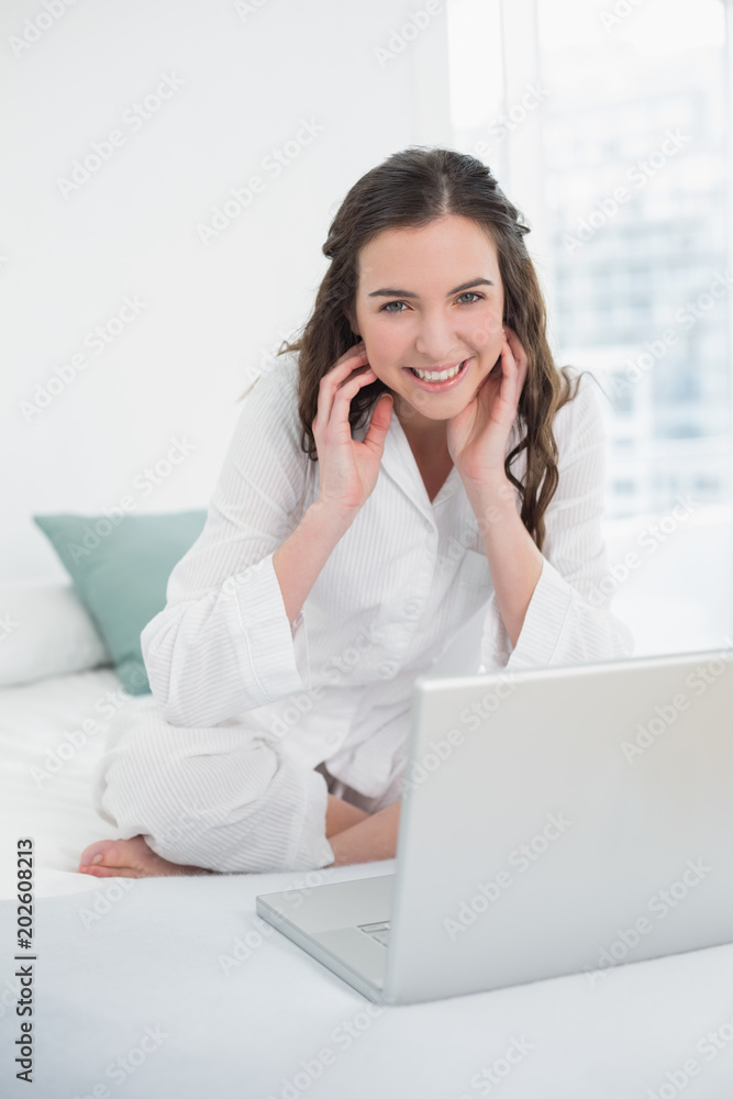 Smiling casual brunette with laptop sitting in bed Smiling casual brunette with laptop sitting in bed