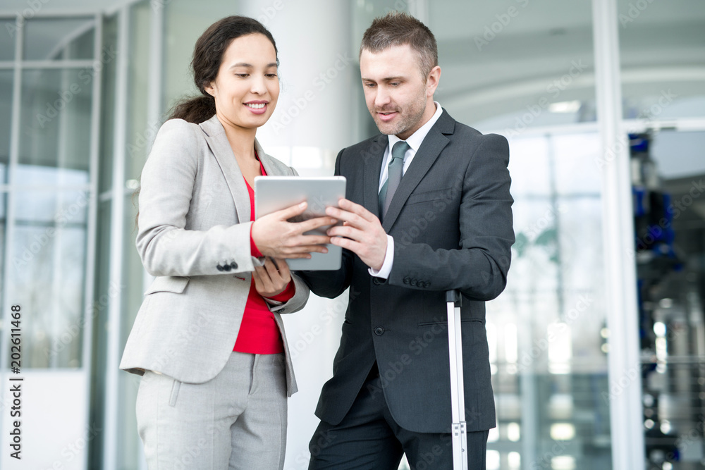 Positive confident multiethnic managers discussing sales and making forecast while analyzing report on tablet in office hall Positive confident multiethnic managers discussing sales and making forecast while analyzing report on tablet in office hall