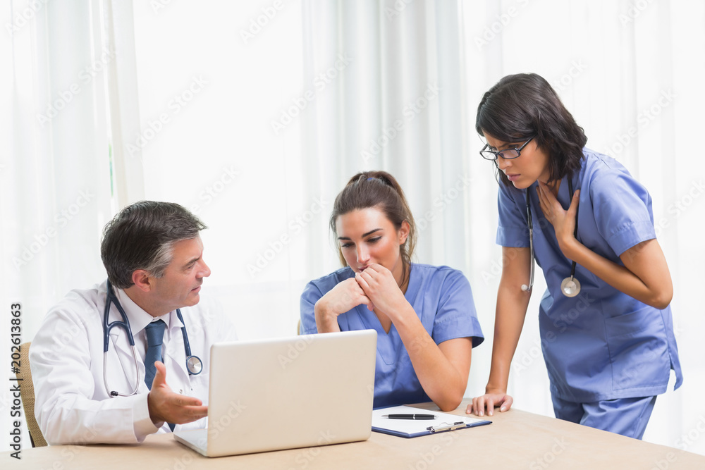 Doctor showing nurses something sad on laptop Doctor showing nurses something sad on laptop