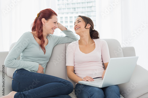 Cheerful female friends using laptop at home