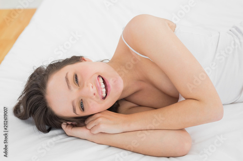 Cheerful pretty young woman lying in bed