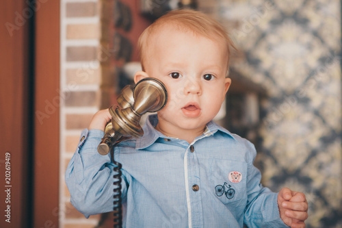 A little blond boy in a blue shirt is calling on the phone photo