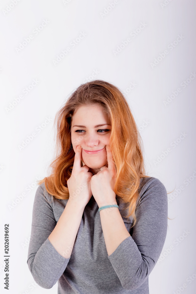 beautiful young woman forcing a smile, holding her fingers near lips beautiful young woman forcing a smile, holding her fingers near lips