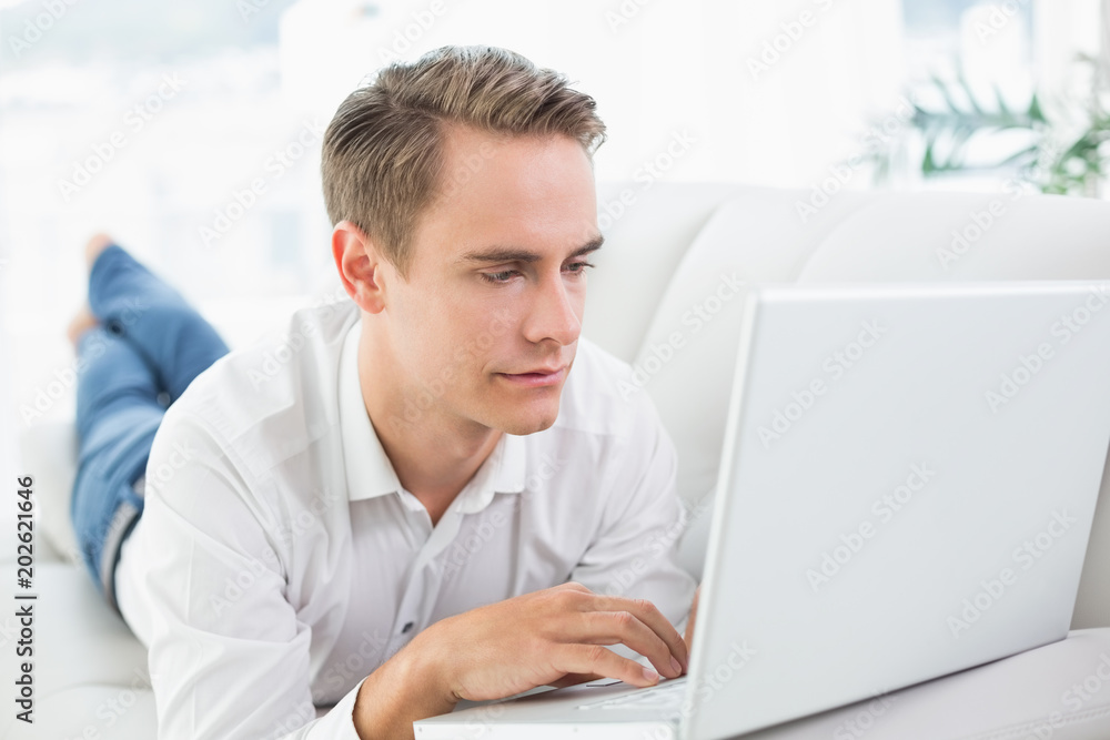 Relaxed casual man using laptop while lying on sofa Relaxed casual man using laptop while lying on sofa