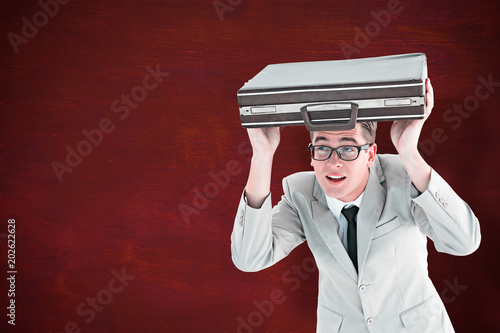 Geeky businessman holding his briefcase over head against desk