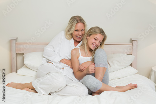 Happy mother tickling daughter in bed