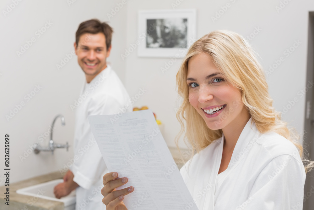 Smiling woman holding document with man in kitchen Smiling woman holding document with man in kitchen