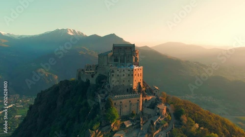 Aerial: drone flying at old medieval abbey perched on mountain top, background snowy Alps at sunrise. Sacra di San Michele (italian) - Saint Michel Abbey (english traslation) - Turin, Italy photo
