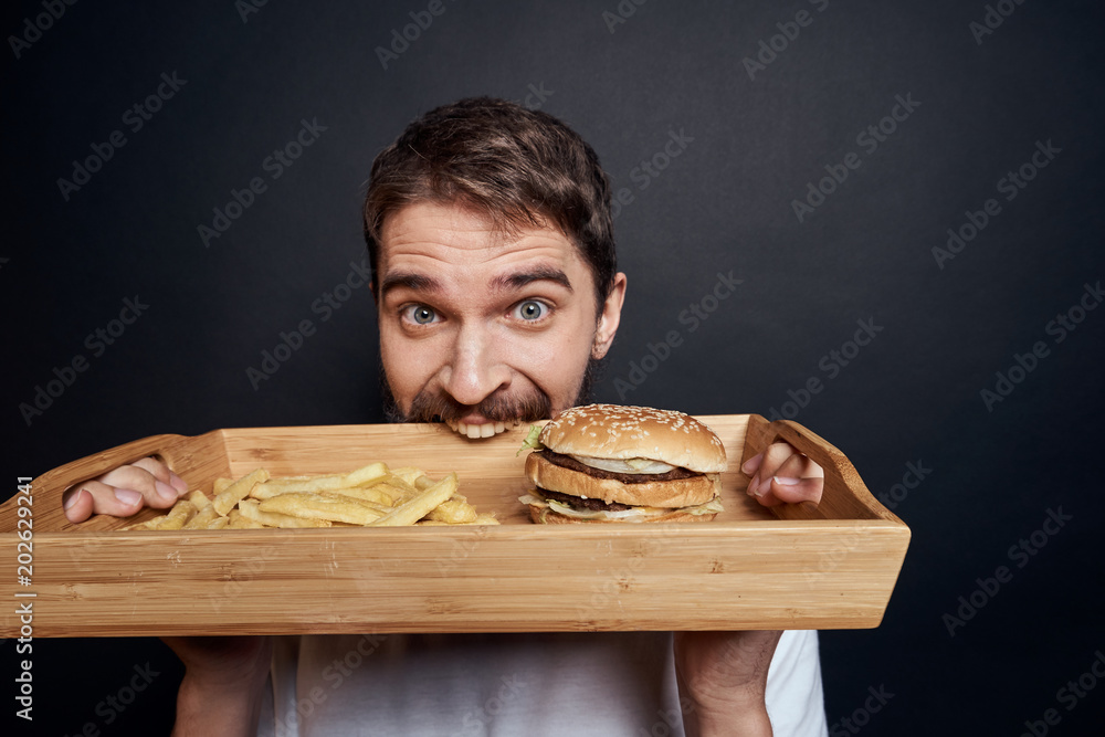 man gnaws a tray with a hamburger and french fries man gnaws a tray with a hamburger and french fries