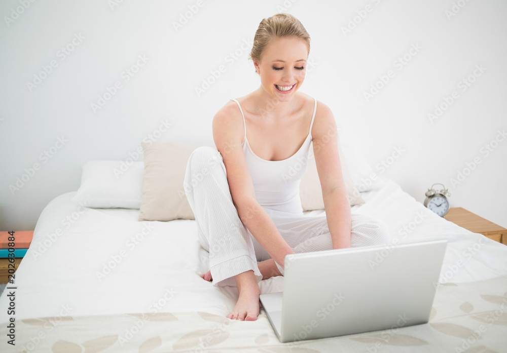 Natural happy blonde looking at laptop while sitting on bed Natural happy blonde looking at laptop while sitting on bed