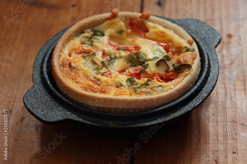 Tomato and spring onion quiche in a cast iron pot dish on a wood background