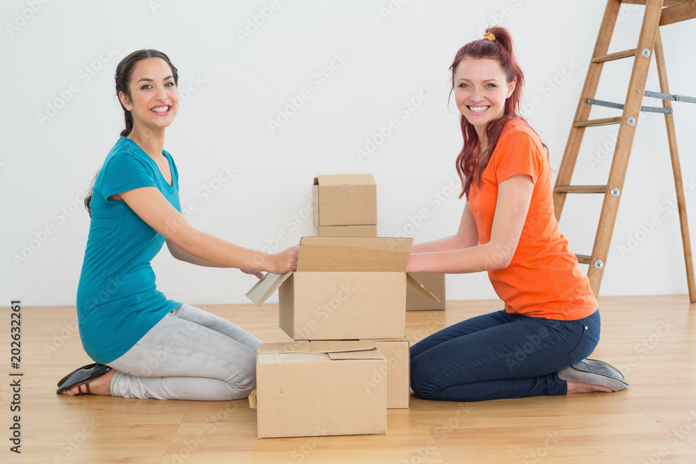 Happy friends unwrapping boxes in a new house Happy friends unwrapping boxes in a new house