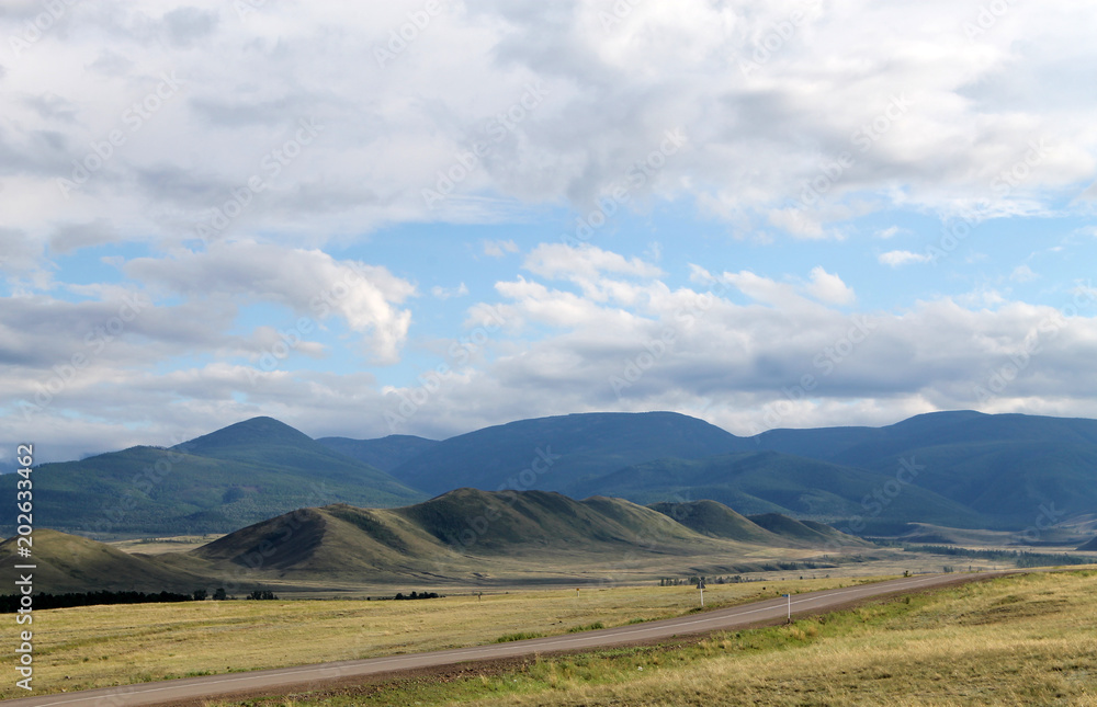Wide steppe with yellow grass under a blue sky with white clouds Sayan mountains Siberia Russia