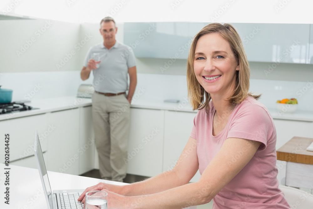 Woman using laptop while man drinking water in kitchen Woman using laptop while man drinking water in kitchen