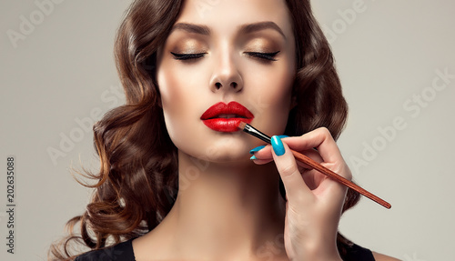 Makeup artist applies  red lipstick  . Beautiful woman face. Hand of make-up master, painting lips of young beauty  model girl . Make up in process