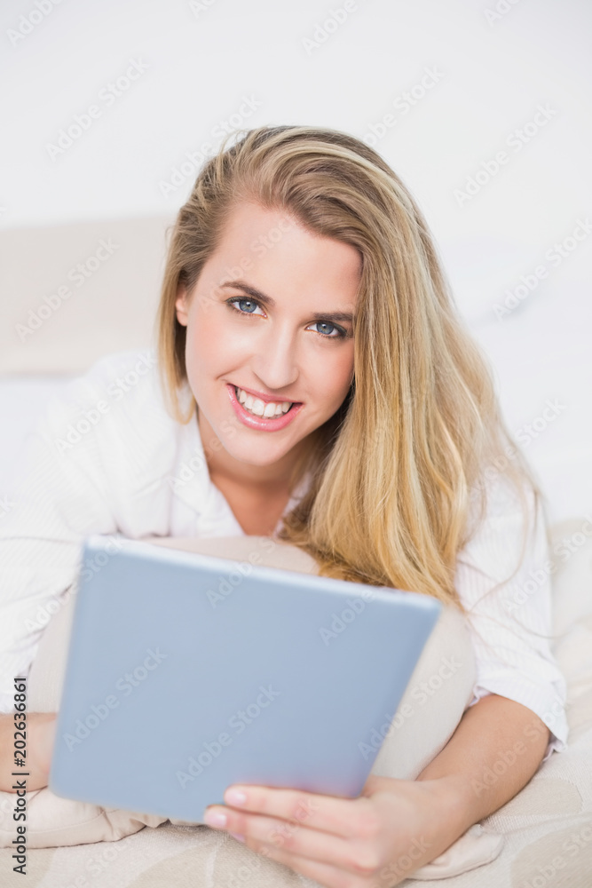 Smiling model using her tablet lying on cosy bed Smiling model using her tablet lying on cosy bed