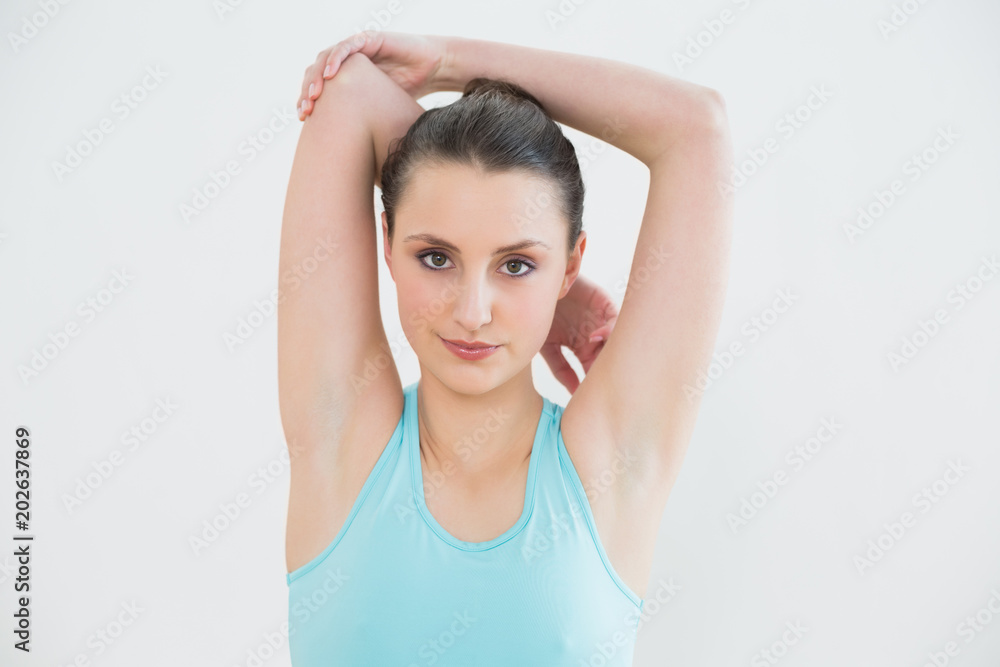 Toned woman stretching hands behind head against wall