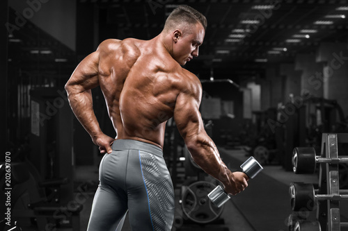 Rear view muscular man showing back in gym. Strong male bodybuilder, working out photo