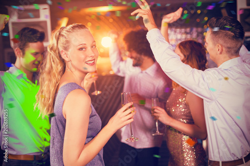 Woman holding glass of champagne while dancing with friends against flying colours