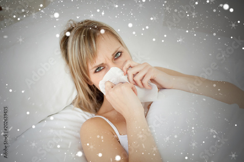 Composite image of sick blonde woman blowing lying on her bed against snow