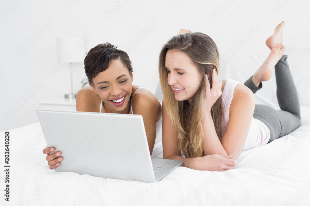 Cheerful relaxed female friends using laptop in bed Cheerful relaxed female friends using laptop in bed