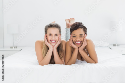 Smiling young female friends lying in bed