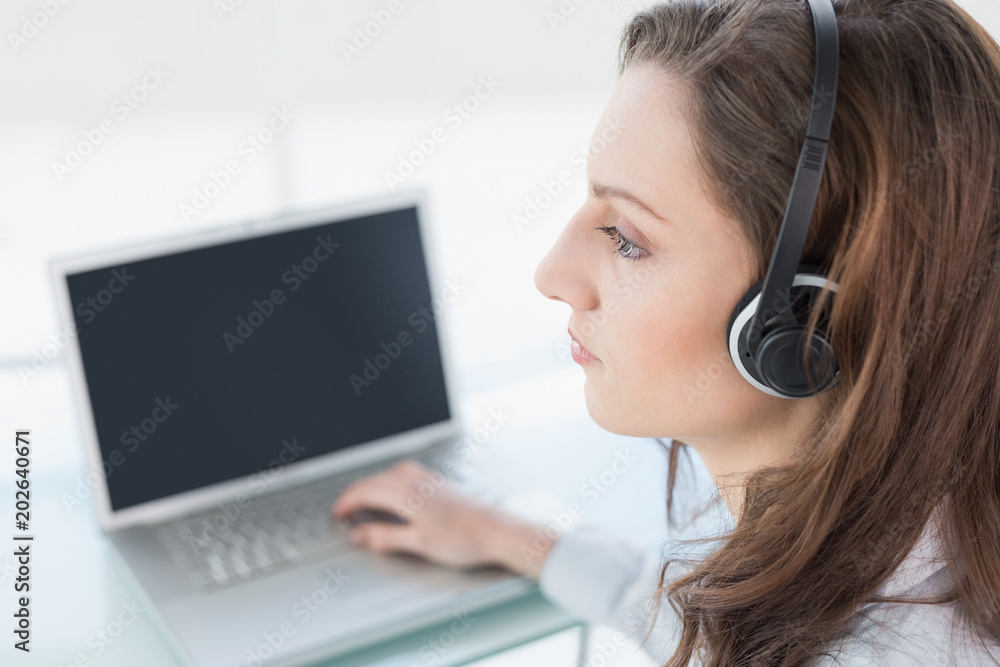 Serious businesswoman wearing headset in front of laptop Serious businesswoman wearing headset in front of laptop