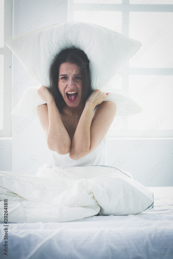 Young caucasian woman covering her head and ears with pillows Young caucasian woman covering her head and ears with pillows