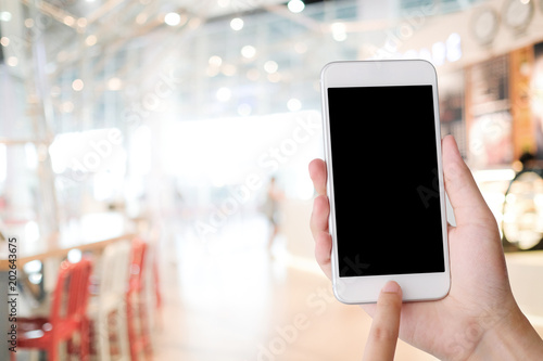 Hand holding smart phone with blank screen over blur cafe background  mock up  template  restaurant reservation  food online  food delivery concept