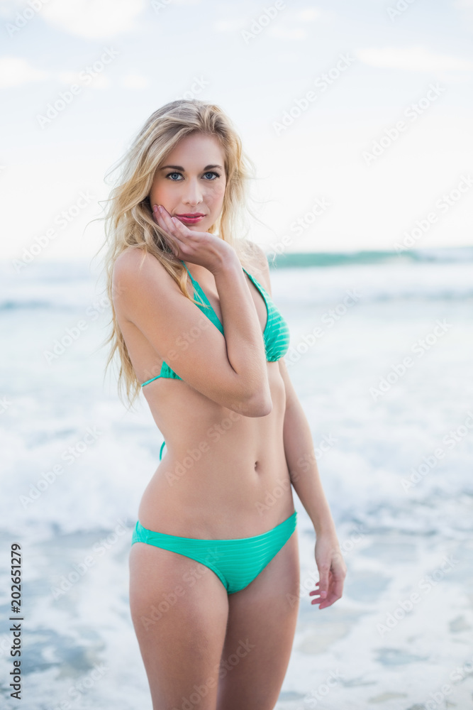 Cute blonde woman in green bikini posing holding her head